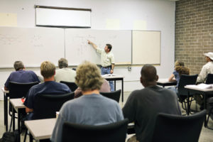An adult education teacher pointing to an electrical circuit on the board.