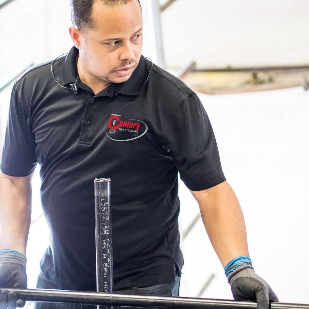A man wearing a black shirt is engaged in metalworking, manipulating a metal bar with tools.